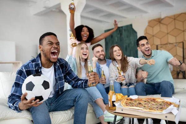 Emocjonalni, wielorasowi przyjaciele oglądają mecz piłki nożnej razem w domu, krzycząc GOAL, świętując zwycięstwo — Zdjęcie stockowe