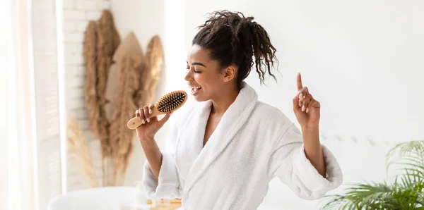 Noir dame chantant tenant brosse à cheveux comme microphone dans salle de bain, panorama — Photo