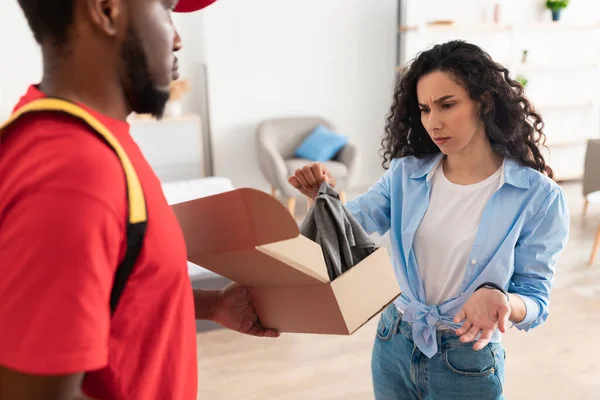 Verwirrte frustrierte Dame packt Karton aus und hält Kleidung in der Hand — Stockfoto