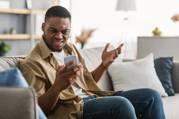 Недовольный черный человек с помощью смартфона Чтение негативного сообщения дома — стоковое фото