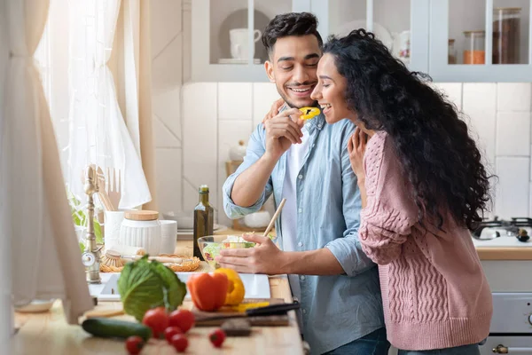 Ung arabisk kvinna provsmaka mat medan matlagning med make i köket tillsammans — Stockfoto