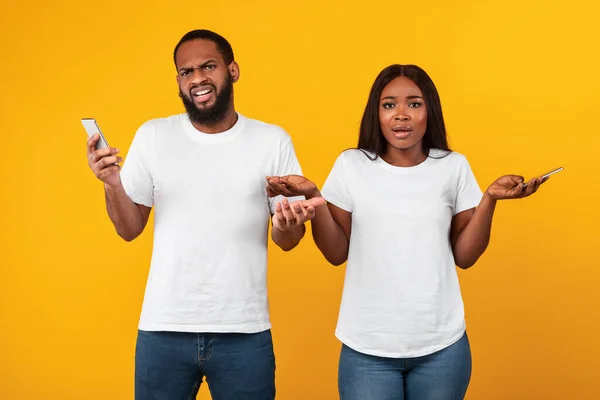 Confused sad millennial african american couple holding their phones