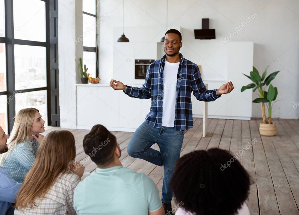 Happy black guy showing pantomime to his multiracial friends, playing charades guessing game at home