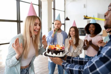 Çok ırklı arkadaşlar heyecanlı sarışın doğum günü bayanı için sürpriz yapıyorlar, elinde mumlarla pasta tutuyorlar, evde parti veriyorlar.