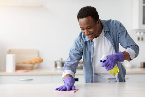 Smiling black guy cleaning kitchen furniture, copy space