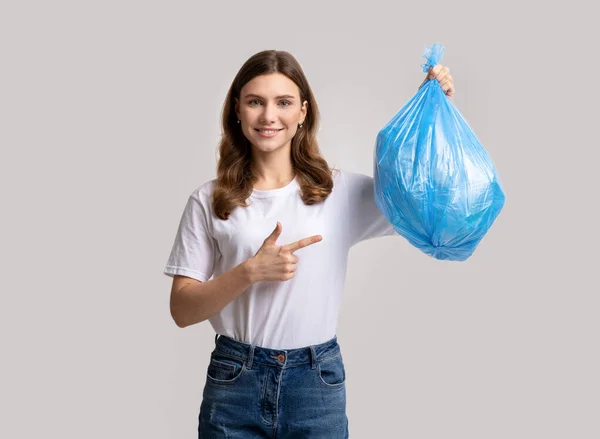 Ritratto di bella giovane donna sorridente che punta al sacchetto di plastica blu della spazzatura — Foto Stock