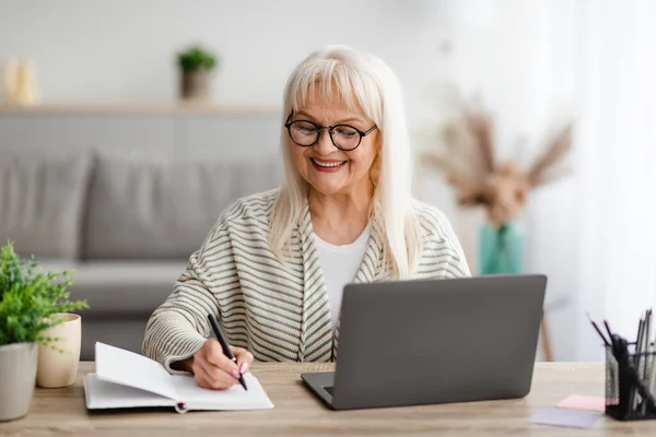 Uśmiechnięta dojrzała kobieta pisząca i korzystająca z laptopa w domu — Zdjęcie stockowe