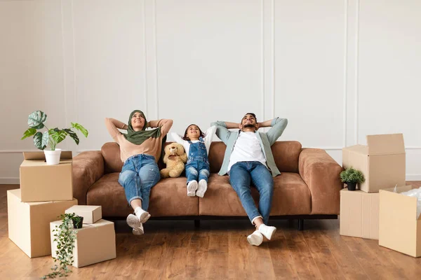 Family relaxing on couch in new home with cardboard boxes