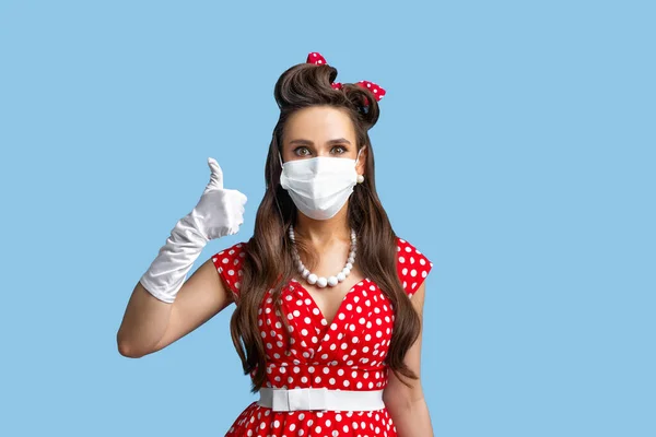 Protecção contra o coronavírus. Pinup mulher em vestido retro usando máscara facial para evitar covid-19, mostrando polegares para cima — Fotografia de Stock