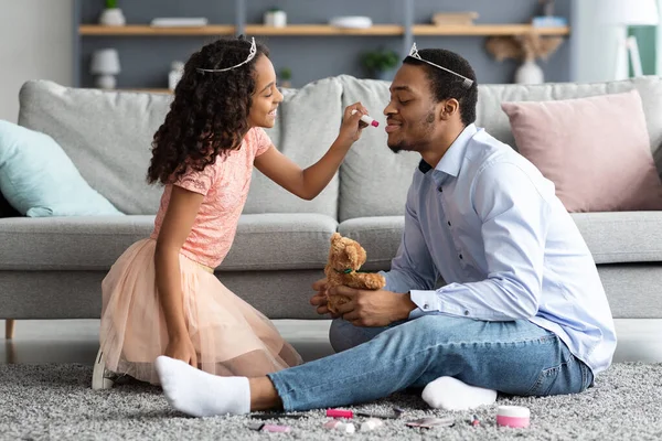 Linda menina negra filha colocando maquiagem em seu rosto pai — Fotografia de Stock