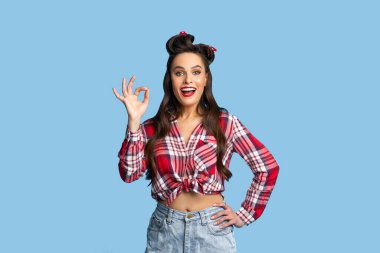 Seksi retro kıyafetli genç bir kadın. Mavi stüdyo arka planında güzel bir jest yapıyor.