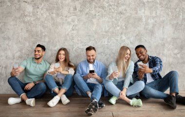 Modern akıllı telefonlu bin yıllık öğrenciler Grey Stüdyoları 'nın yanında oturmuş birbirleriyle iletişim kuruyorlar.