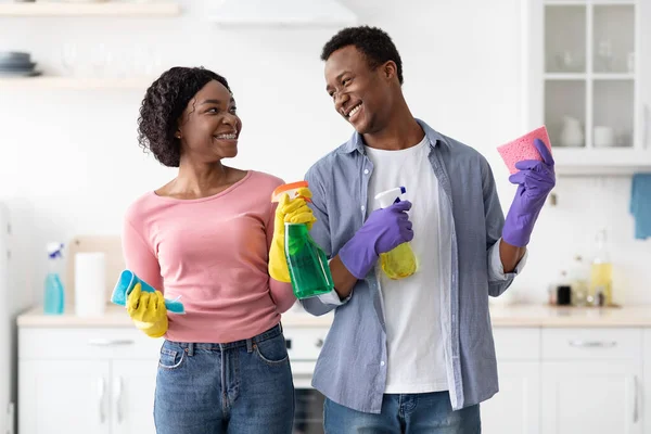 Casal preto positivo com suprimentos para limpeza posando na cozinha — Fotografia de Stock