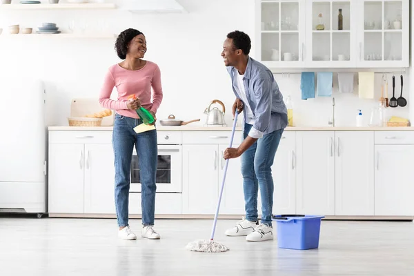Веселый черный мужчина и женщина веселятся во время уборки кухни — стоковое фото
