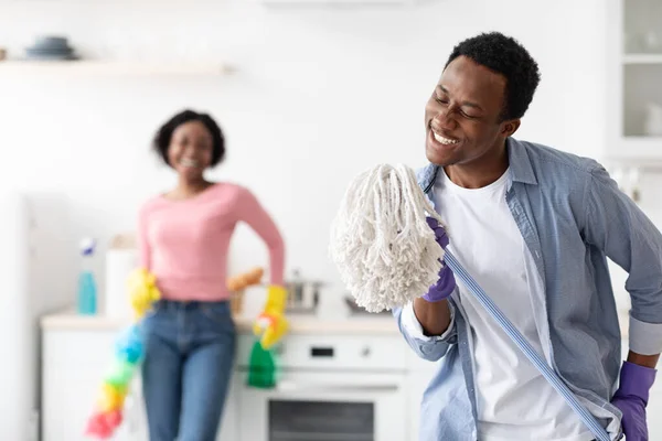 Joyful zwarte man met behulp van dweil als microfoon, zingen tijdens het schoonmaken — Stockfoto