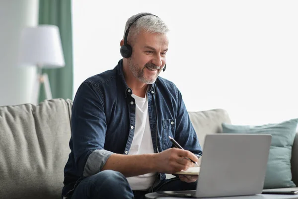 Spännande mogen man studerar online, med hjälp av bärbar dator och headset — Stockfoto