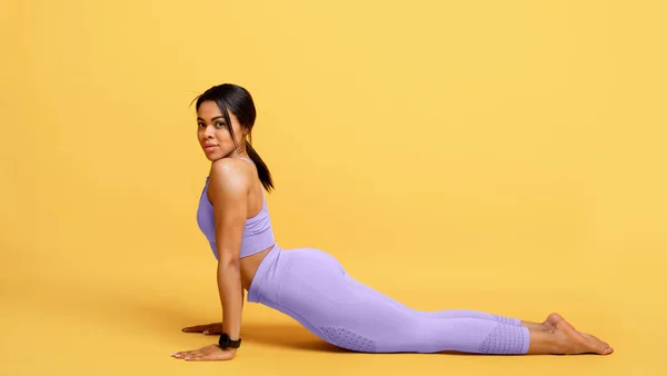Addestramento donna afroamericana, fare esercizio di stretching posteriore su sfondo giallo studio, panorama — Foto Stock