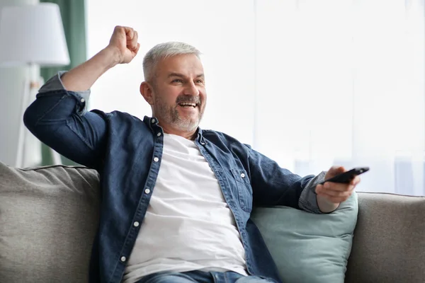 Homem idoso barbudo emocional assistindo TV em casa — Fotografia de Stock