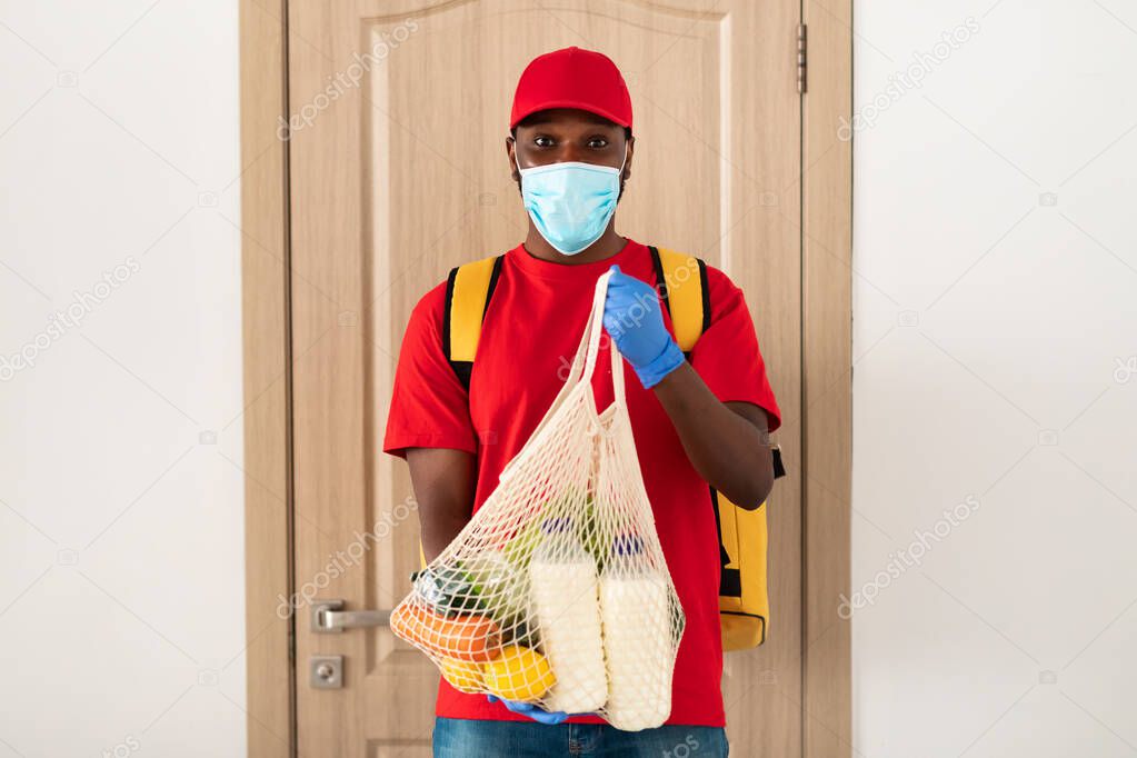 Black delivery man holding eco mesh bag with groceries