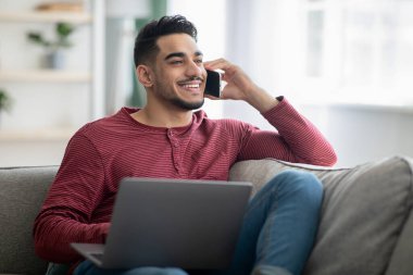 Bilgisayarı ve cep telefonunu kullanarak çalışan Ortadoğulu bir adam.