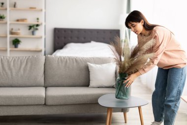 Masaya vazo ve kurumuş çiçek çimi koyan kadın.