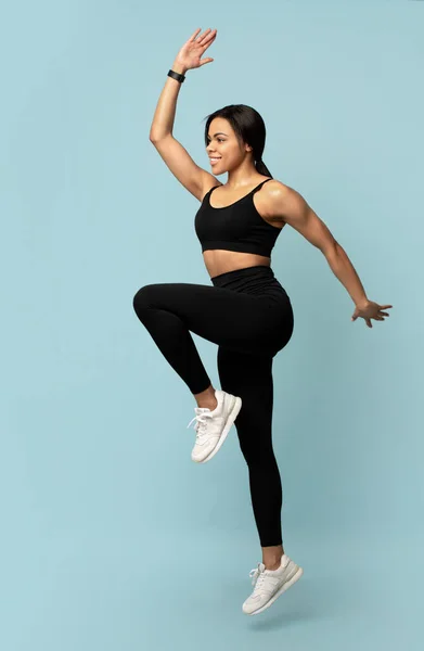 Concepto deportivo. Joven mujer afroamericana saltando, ejercitando y levantando la pierna sobre fondo azul —  Fotos de Stock