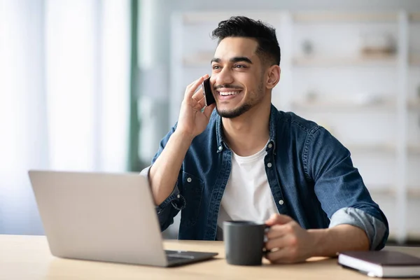 Chico árabe feliz freelancer trabajando desde casa, teniendo conversación telefónica — Foto de Stock