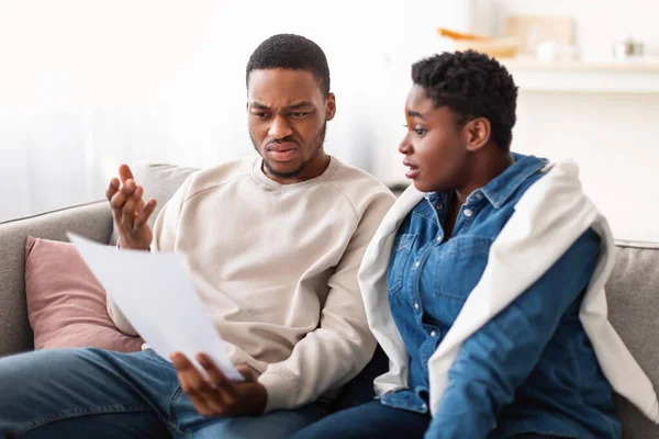 Confused black couple reading documentation at home, sitting on couch — Stock Photo, Image