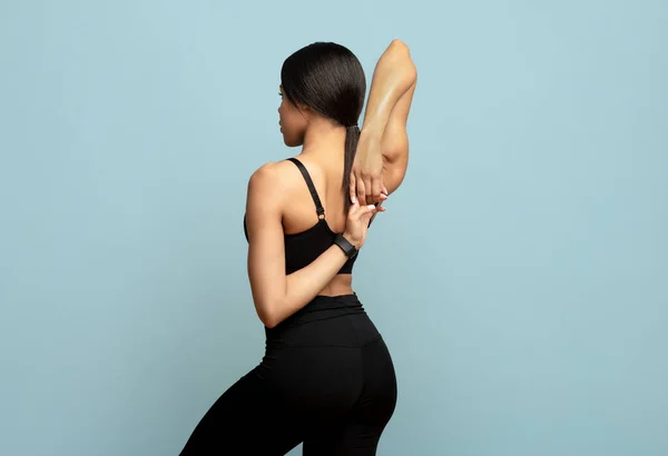 Joven mujer negra en ropa deportiva calentándose antes de entrenar, uniendo las manos detrás de su espalda sobre fondo negro azul —  Fotos de Stock