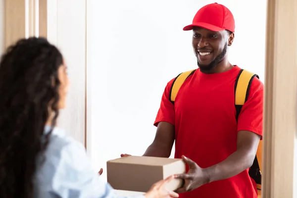 Schwarzer Zusteller hält Schachtel in der Hand und gibt sie dem Kunden — Stockfoto