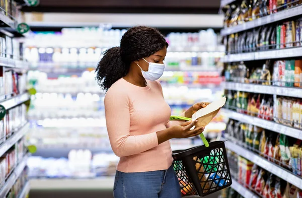 Υπέροχη Αφροαμερικανή γυναίκα με μάσκα προσώπου που κάνει επιλογή των προϊόντων στο σούπερ μάρκετ κατά τη διάρκεια του κλείδωμα coronavirus — Φωτογραφία Αρχείου