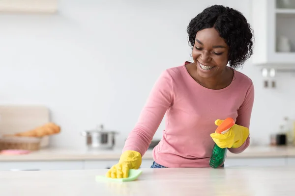 Fröhliche afrikanisch-amerikanische junge Frau in Gummihandschuhen putzt Tisch — Stockfoto