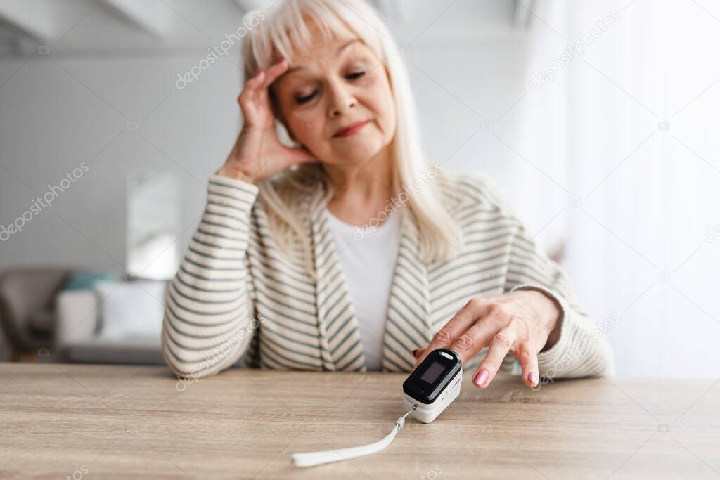 Senior woman using Oximeter at home. Healthcare Concept