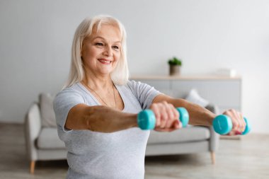 İki dambılla evde egzersiz yapan olgun bir kadın.