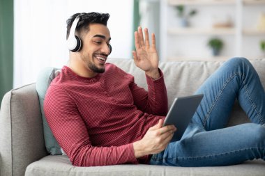 Genç adam dijital tablet kullanarak arkadaşlarıyla görüntülü görüşme yapıyor.