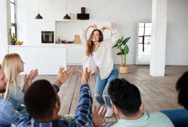 Grappige jonge dame spelen charades met haar vrienden, genieten van leuke spel, tonen woord met pantomime thuis — Stockfoto