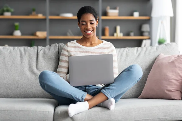 Carrera independiente. Joven sonriente dama negra trabajando con el ordenador portátil en casa —  Fotos de Stock