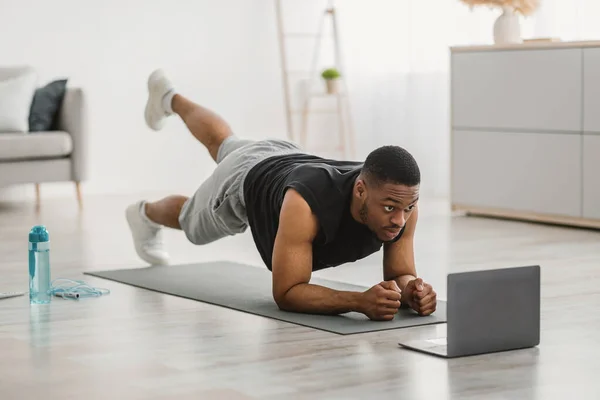 Afrikansk man tränar på laptop gör Plank Ben höjer inomhus — Stockfoto