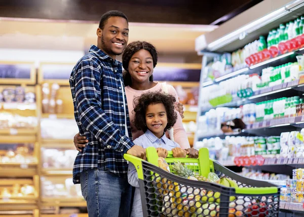 Portret radosnej afroamerykańskiej rodziny z uroczą córką pozowanie i uśmiech przed kamerą w dużym supermarkecie — Zdjęcie stockowe