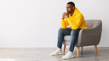 Düşünceli siyahi adam Gri arka plan yerine Sandalyede oturmayı düşünüyor.