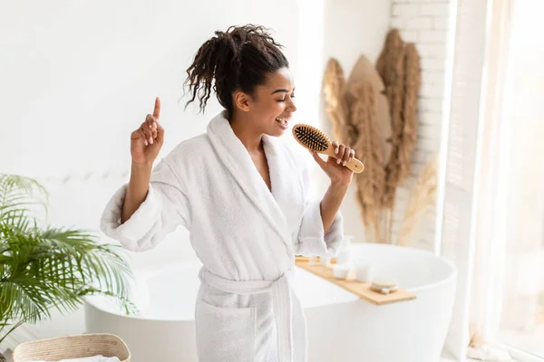 Alegre dama afroamericana cantando con cepillo de pelo en baño moderno —  Fotos de Stock