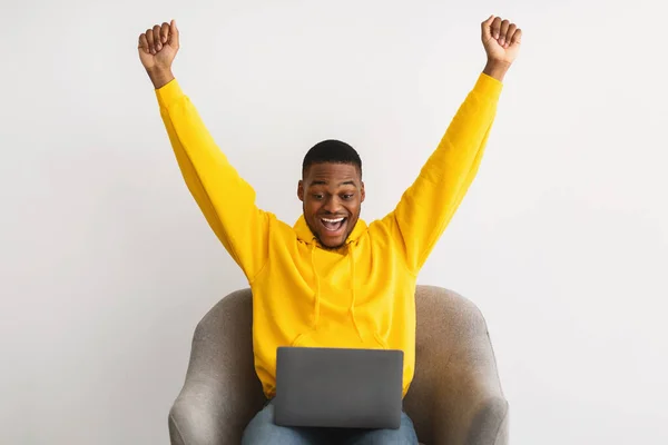 Opgewonden Afrikaanse man op zoek naar laptop schudden vuisten, grijze achtergrond — Stockfoto