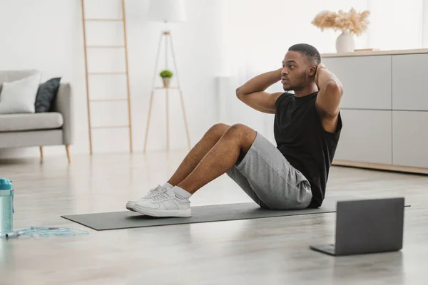 Uomo nero sportivo che fa esercizio Sit-Ups al computer portatile al coperto, vista laterale — Foto Stock