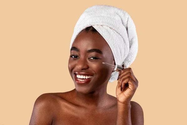 Черная женщина наносит увлажняющий крем или гиалуроновую кислоту на лицо — стоковое фото