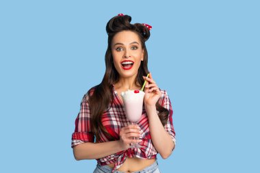 Eski moda giyinmiş çekici bir kadının portresi mavi arka planda milkshake içerken kendini mutlu hisseder.