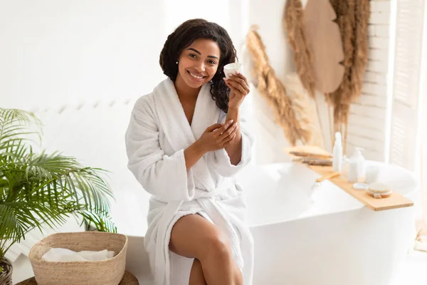 Zwarte dame toepassen crème op handen hydraterende huid in de badkamer — Stockfoto
