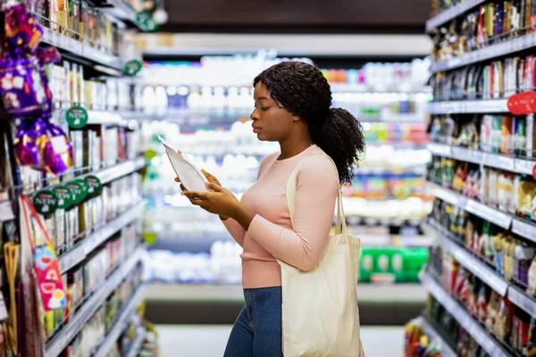 食品のラベルを読んでエコバッグとかなり黒の女性,ショッピングモールで食料品 — ストック写真