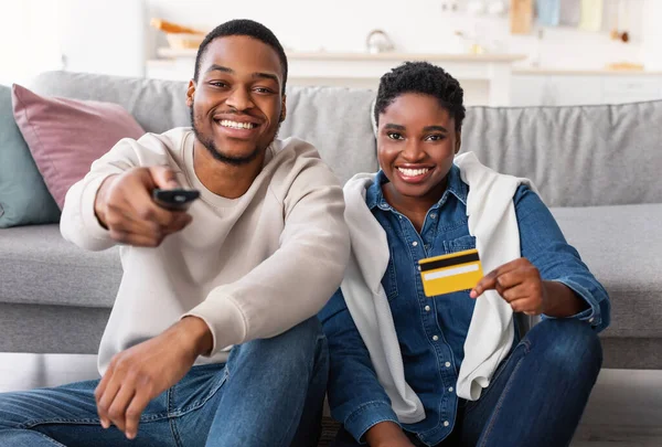 Afro pár držící dálkové ovládání a debetní kreditní karty — Stock fotografie