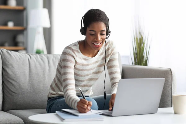Ensino à Distância. Sorrindo senhora africana no fone de ouvido estudando com computador em casa — Fotografia de Stock