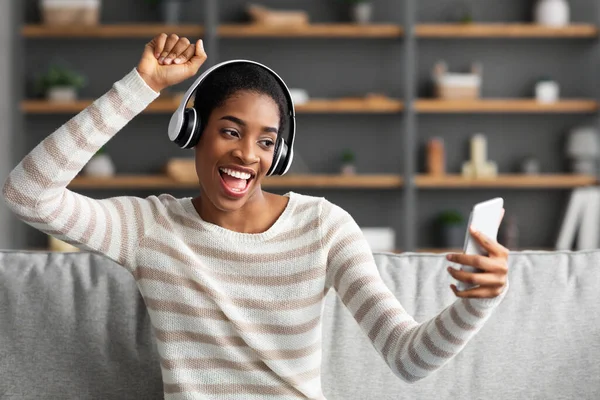 Kedvenc lejátszási lista. Vidám afrikai nő zenét hallgat okostelefonnal és vezeték nélküli fülhallgatóval — Stock Fotó